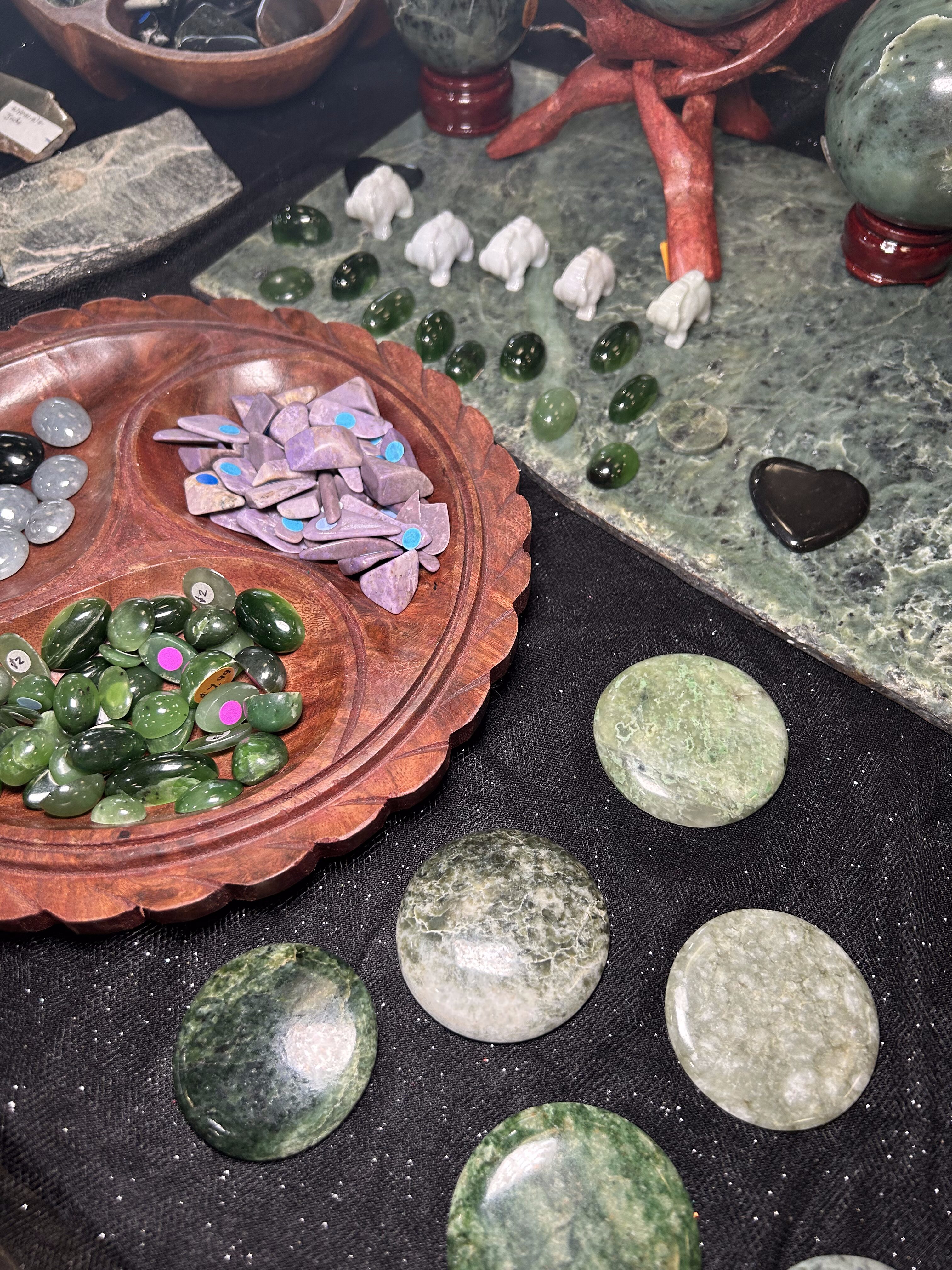 Table with small pieces of Jade crystal on it. There's circular green pieces of jade, small green pieces, and purple pieces. Some are sitting in a decorative bowl.