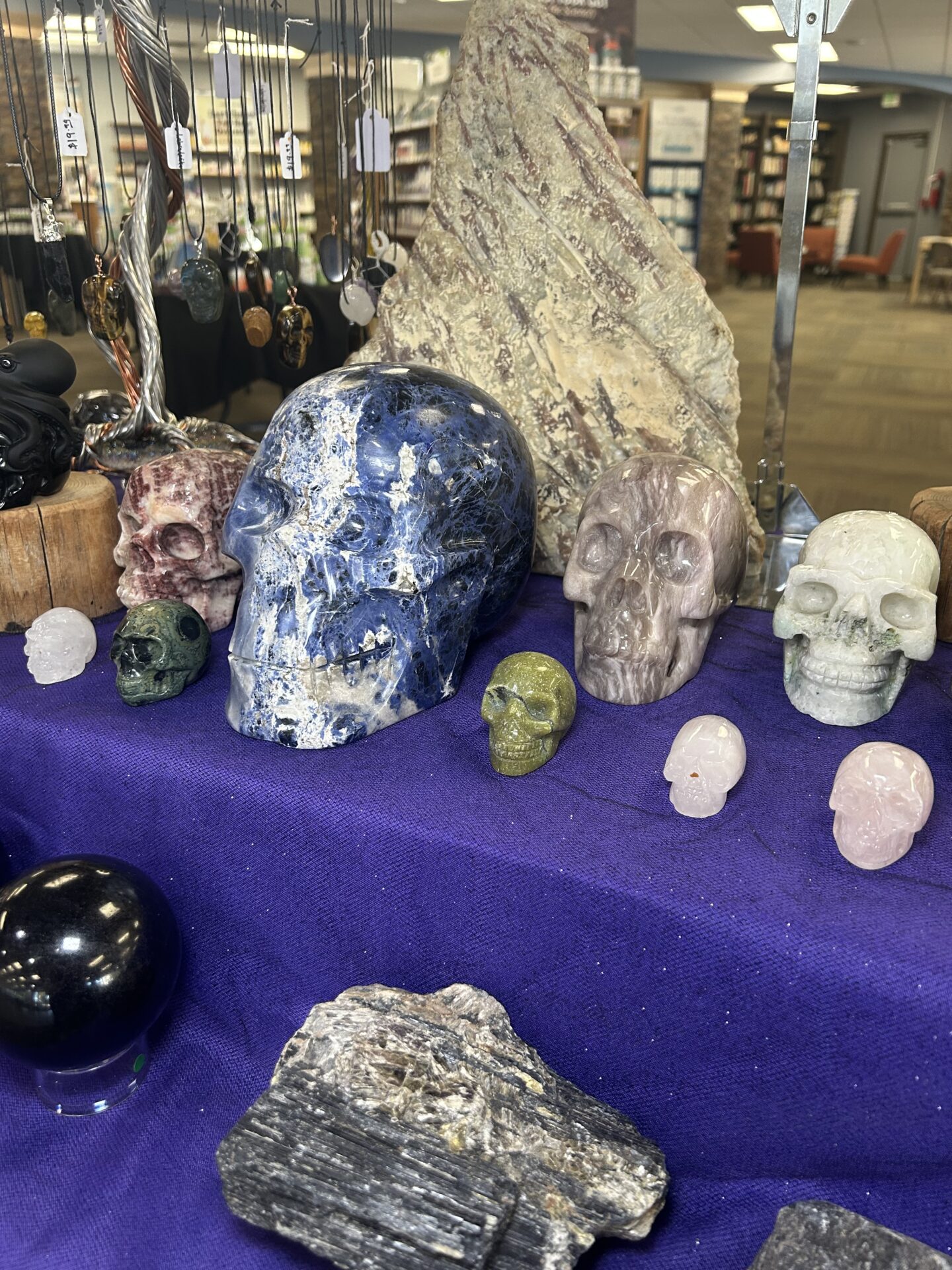 Stone skulls sitting on a purple table cloth. There are also Black Tourmaline stones on the table.